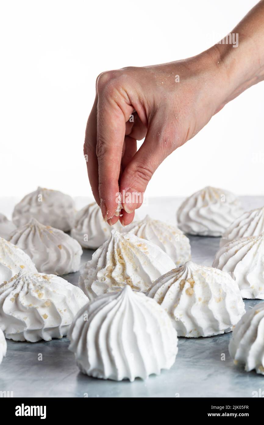 saupoudrer la meringue à la main féminine avec du sucre en poudre. Meringue douce et aérée sur fond blanc avec espace de copie, vue latérale, mise au point sélective. Concept de ho Banque D'Images