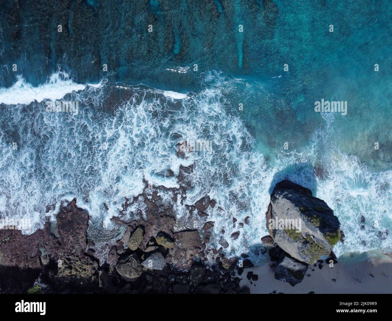 Vue aérienne en bas de l'eau cristalline et des vagues blanches écrasant les roches agaistes de nusa penida Banque D'Images