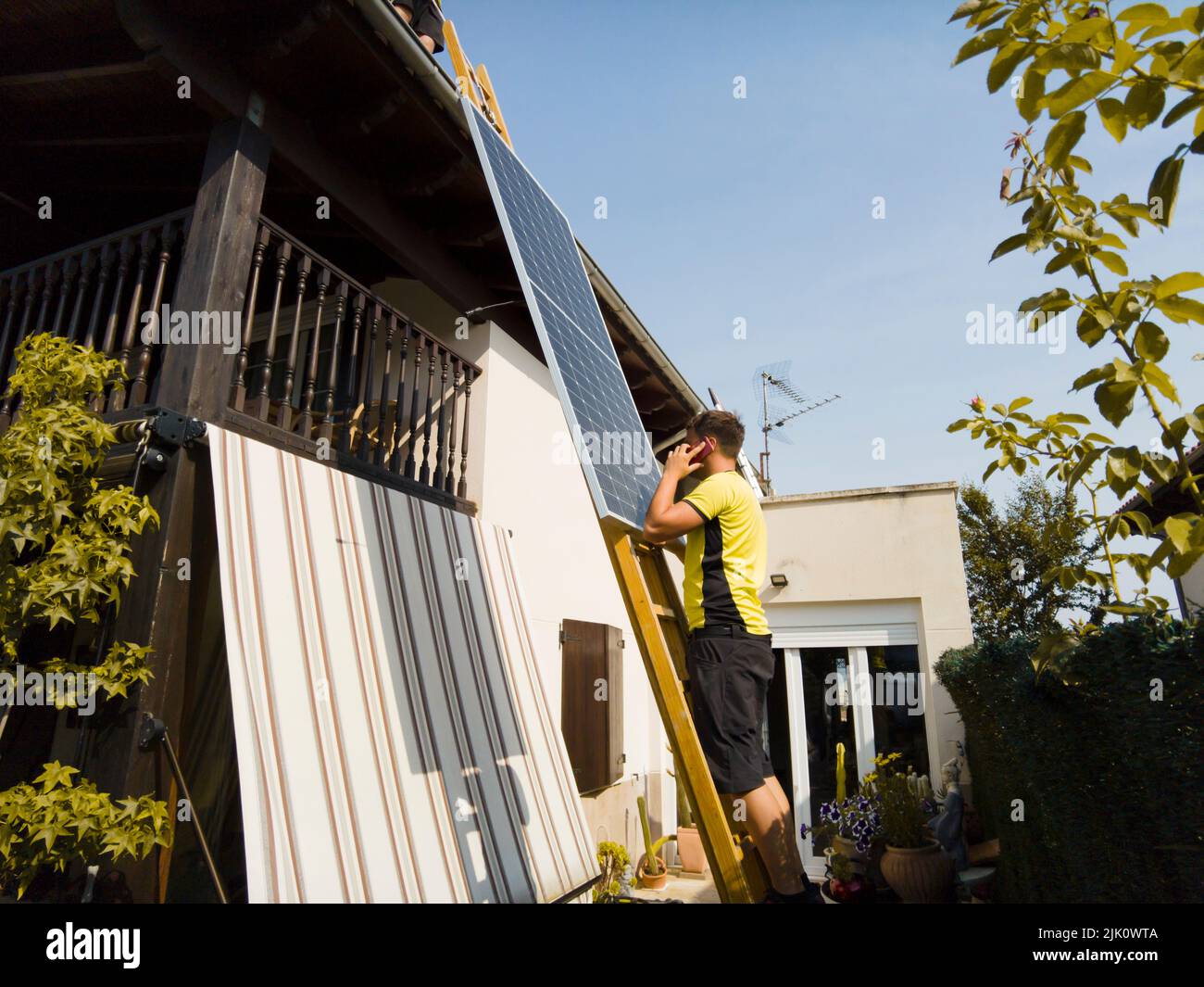 un employé lève le panneau solaire vers le toit, en montant l'échelle. Navarre, Espagne, Europe. Concepts d'environnement et de technologie. Banque D'Images