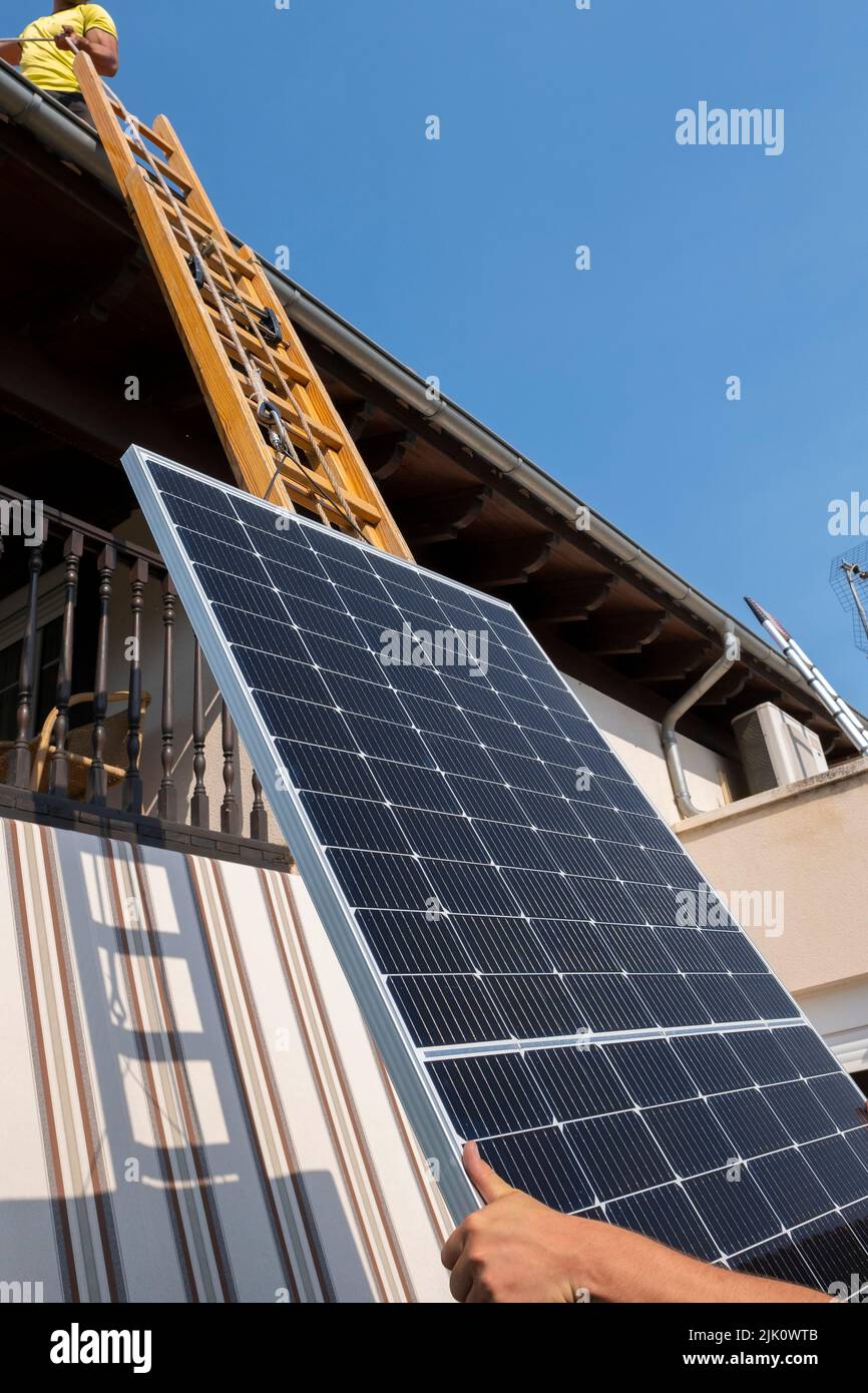 un employé lève le panneau solaire vers le toit, en montant l'échelle. Navarre, Espagne, Europe. Concepts d'environnement et de technologie. Banque D'Images