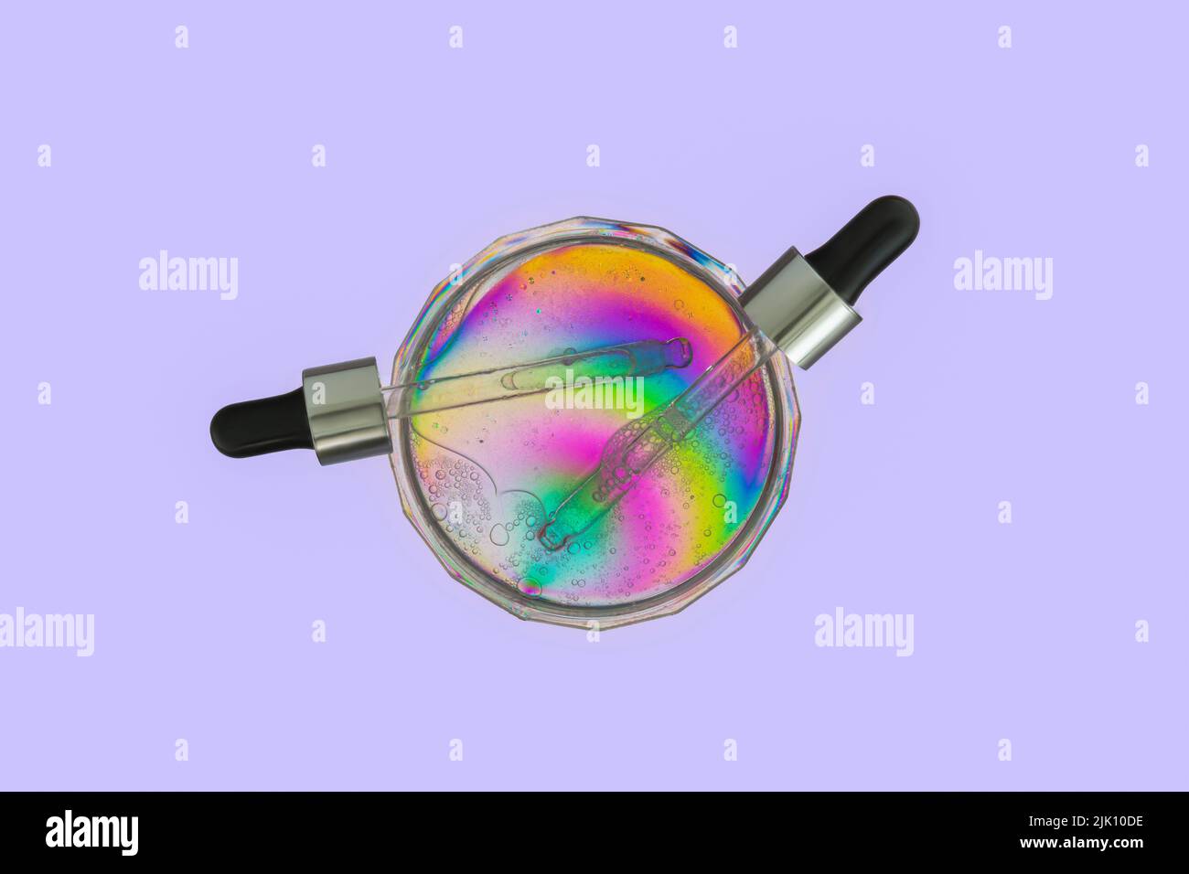 Compte-gouttes de sérum dans une boîte de Petri sur un film plastique arc-en-ciel coloré par photoélasticité isolée sur fond violet clair. Concept futuriste. Banque D'Images