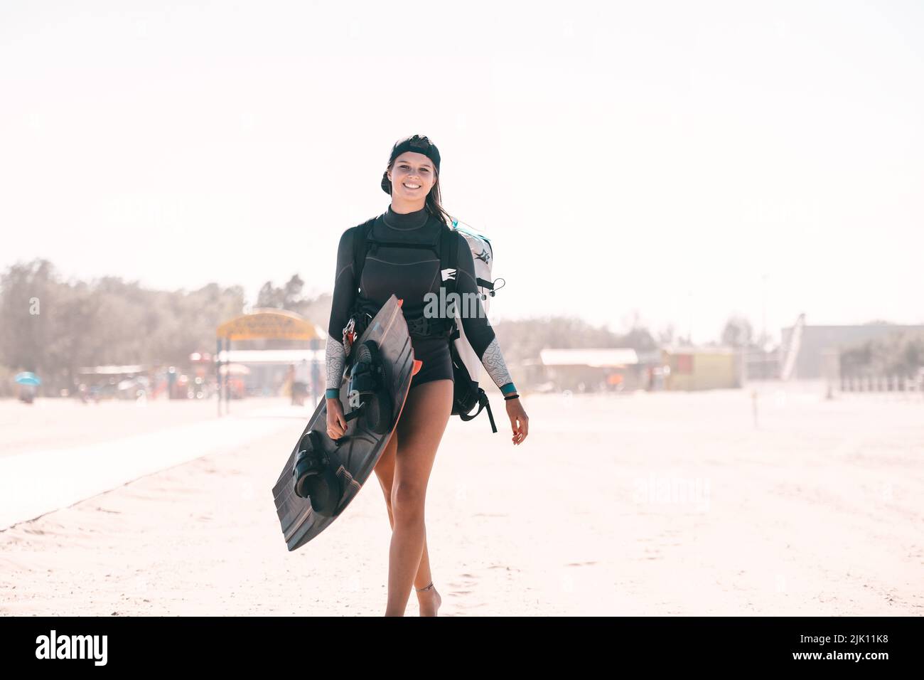 Portrait d'une belle fille souriante posant avec une planche de surf sur la plage et portant un équipement de kitesurf - concept de femme sportive et sport d'été Banque D'Images