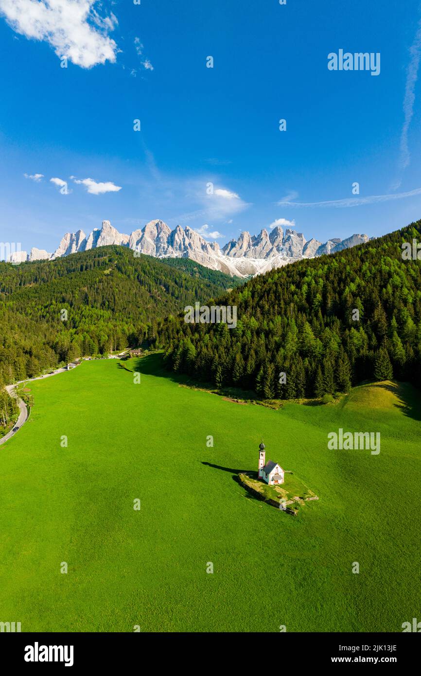 Forêt verte et prairies entourant la petite église de Ranui et Odle au printemps, vue aérienne, vallée de Funes, Dolomites, Tyrol du Sud, Italie, Europe Banque D'Images