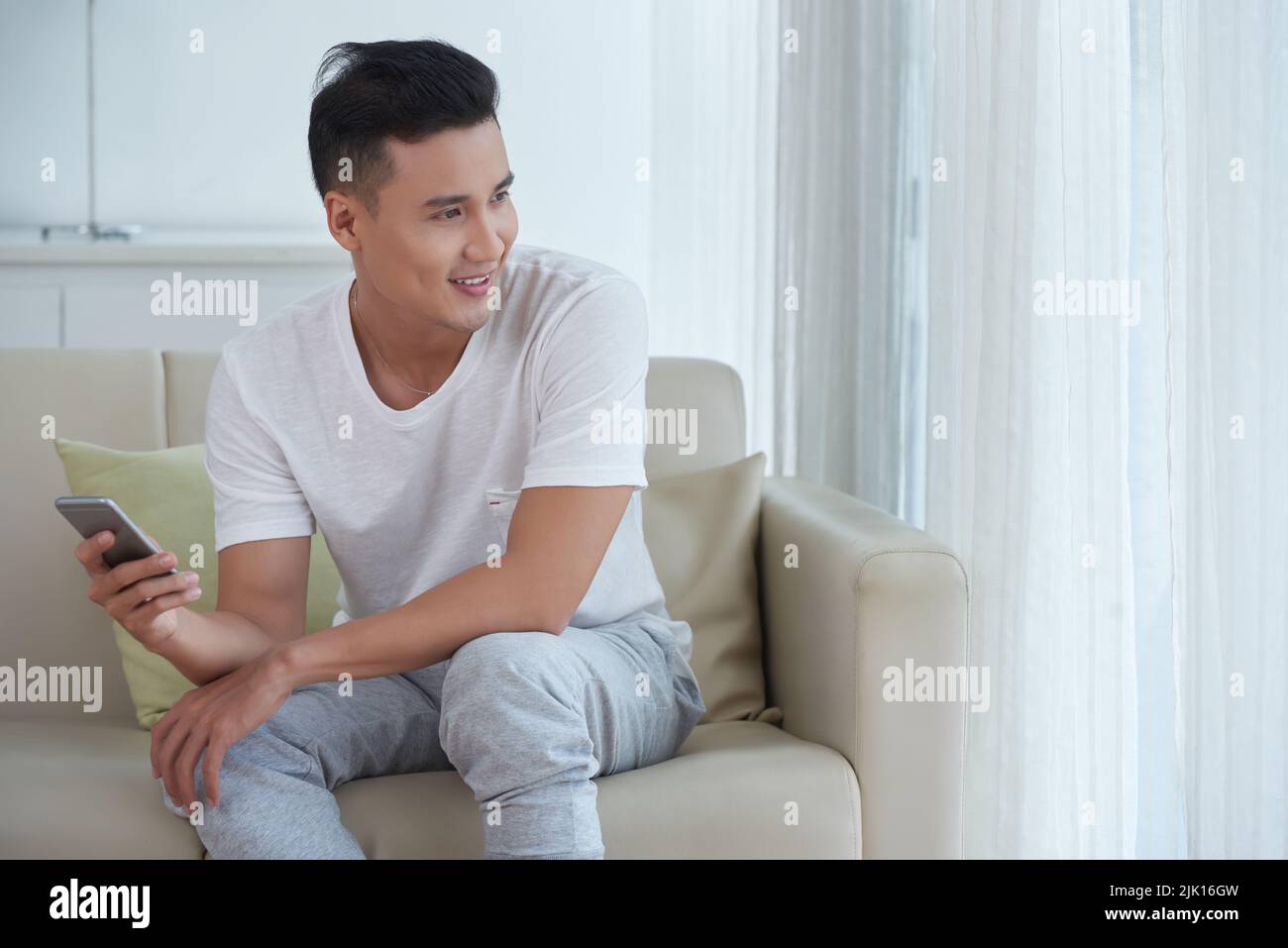 Portrait d'un jeune homme souriant avec un smartphone assis sur son canapé Banque D'Images