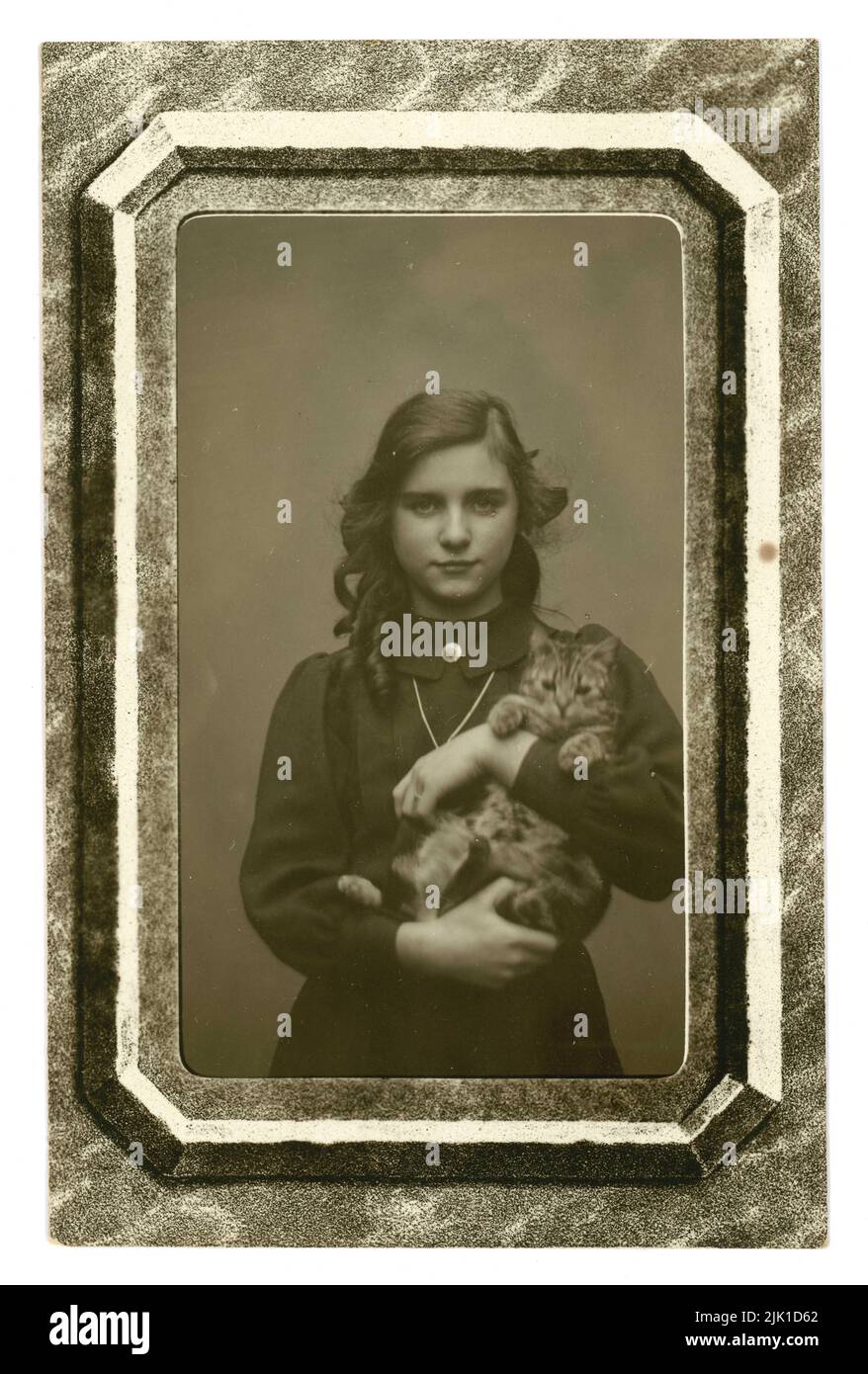 Portrait original de carte postale de l'époque édouardienne de la jolie fille de l'adolescence avec de longs cheveux, tenant son chaton d'animal de compagnie. La carte postale est dotée d'un faux cadre. Écrit au verso est 'avec tous les bons voeux de tous au 24 Charleville Road', daté de Noël 1911 Londres ou Birmingham - Angleterre, Royaume-Uni Banque D'Images