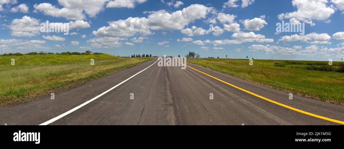 Panorama d'une route à deux voies au sommet d'une rue noire lors d'une journée ensoleillée d'été le long de l'autoroute US 94 dans le comté de Stutsman près de Medina, Dakota du Nord. Banque D'Images