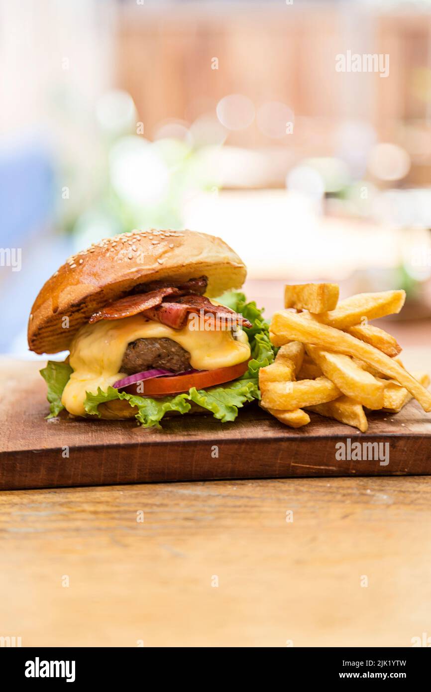 Cheeseburger au fromage, laitue, tomate, oignon, bacon et frites, servi sur une planche de bois dans un restaurant pendant la journée Banque D'Images