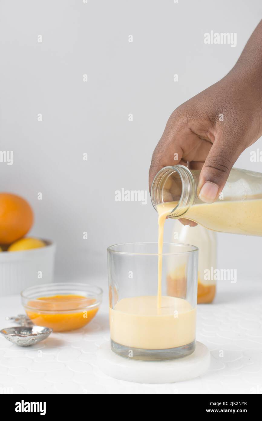Lait versé dans une tasse en verre, main femelle tenant une bouteille de lait versée dans une tasse en verre, lait de mangue versé dans une tasse, lassi de mangue Banque D'Images