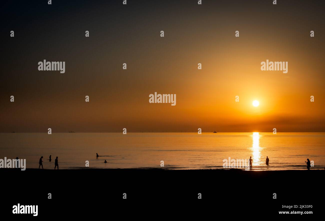 Certaines personnes à la plage pendant un coucher de soleil d'or vif Banque D'Images