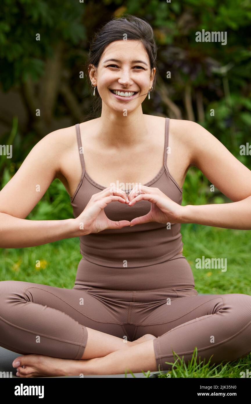 Une bonne santé est une grande nourriture pour votre corps et votre âme. Portrait d'une jeune femme qui fait une forme de coeur avec ses mains tout en faisant de l'exercice à l'extérieur. Banque D'Images