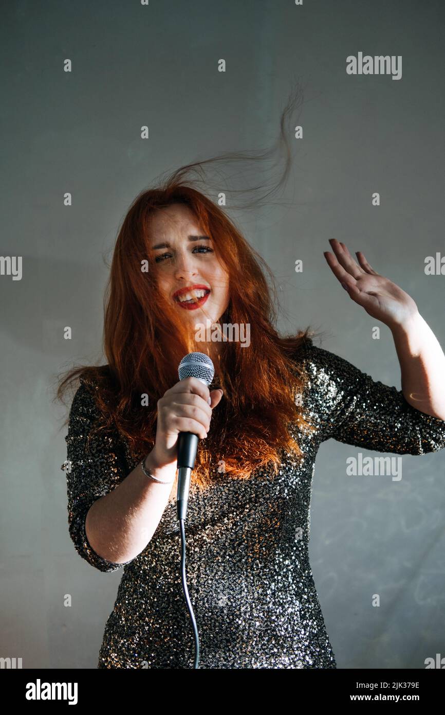 Portrait de femme chanteuse à tête rouge en robe de soirée étincelante tenant un microphone Banque D'Images