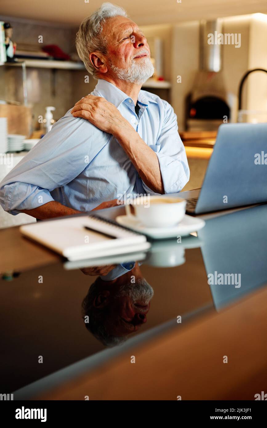 Un homme âgé est assis dans un café et souffre de maux de dos. Banque D'Images