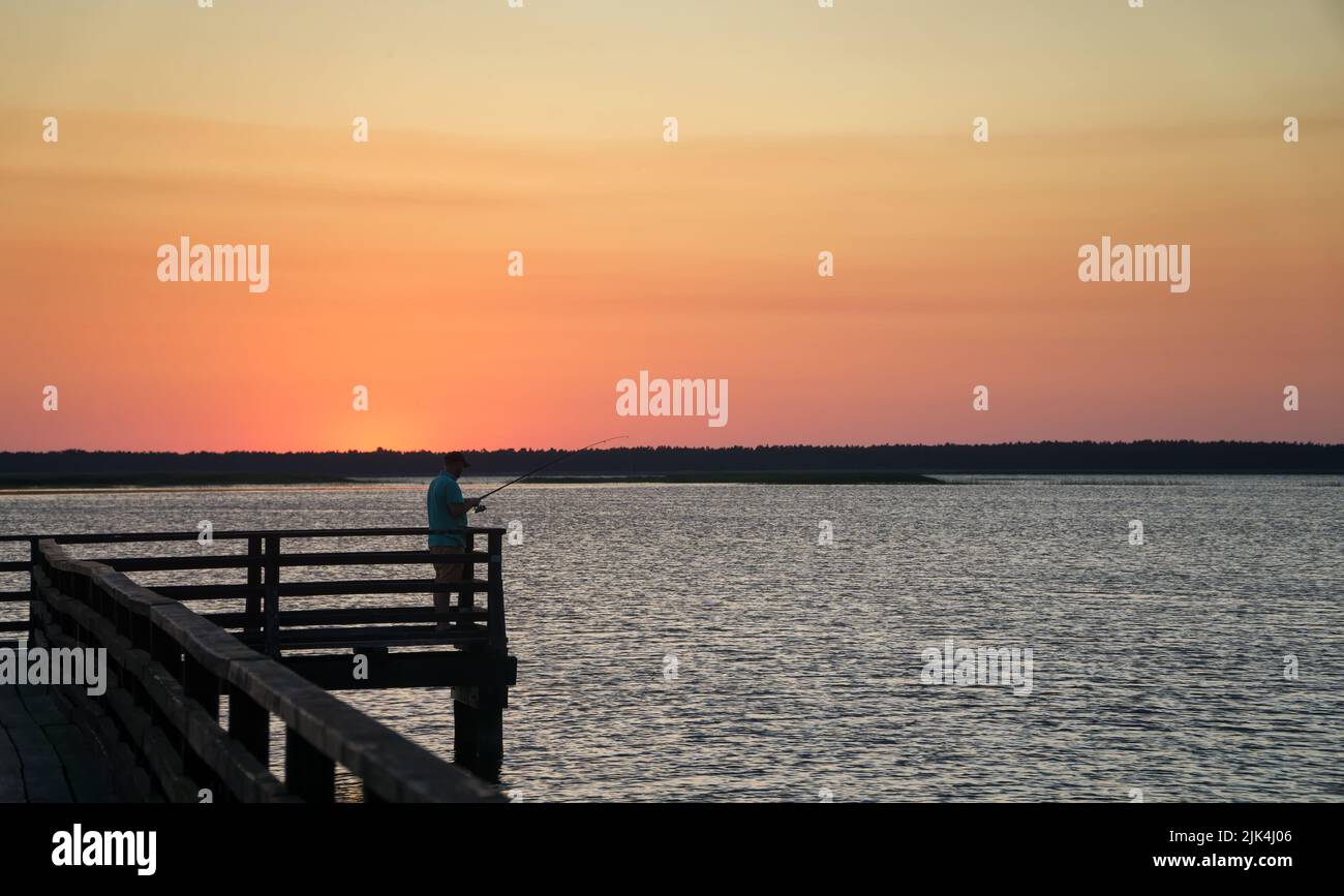 Silhouette de pêcheur sur la jetée au coucher du soleil en été au lac Lebsko, Pomerania, Pologne, Europe. Banque D'Images