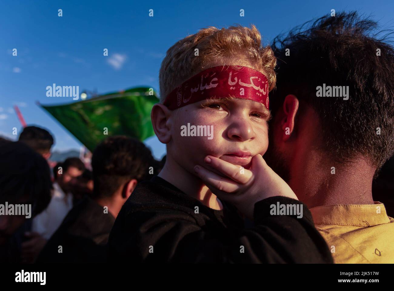 Un garçon musulman chiite cachemirien portant un bandeau avec des  inscriptions islamiques regarde vers les hommes musulmans chiites qui  brandissent des drapeaux religieux et des banderoles au début du Muharram.  Muharram est