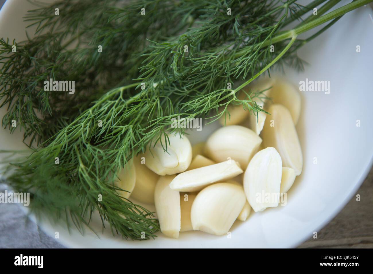 Un bouquet d'aneth vert frais et de gousses d'ail pelées sur une assiette blanche en gros plan. Mise au point sélective. Banque D'Images