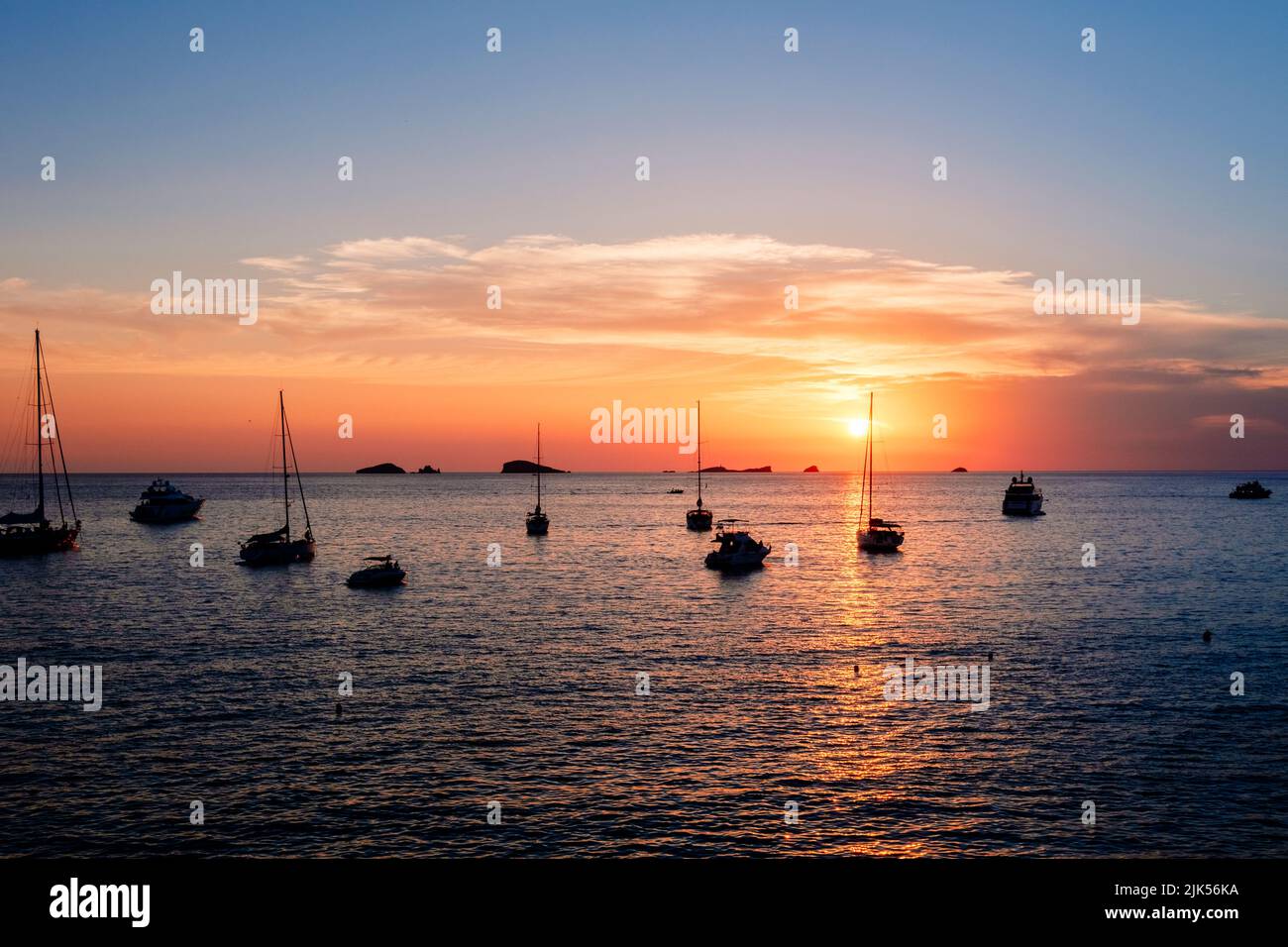 Un coucher de soleil chaud avec le soleil se reflétant sur la surface de la mer, près de la baie avec des bateaux. Banque D'Images