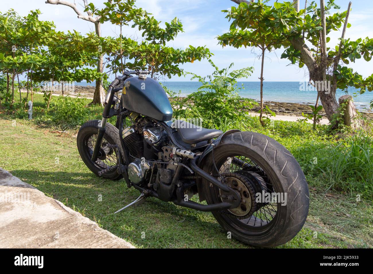 Une moto-hachoir sur mesure garée sur l'herbe à côté d'une plage tropicale. Moto de rat, pilote bas, moteur Honda Banque D'Images