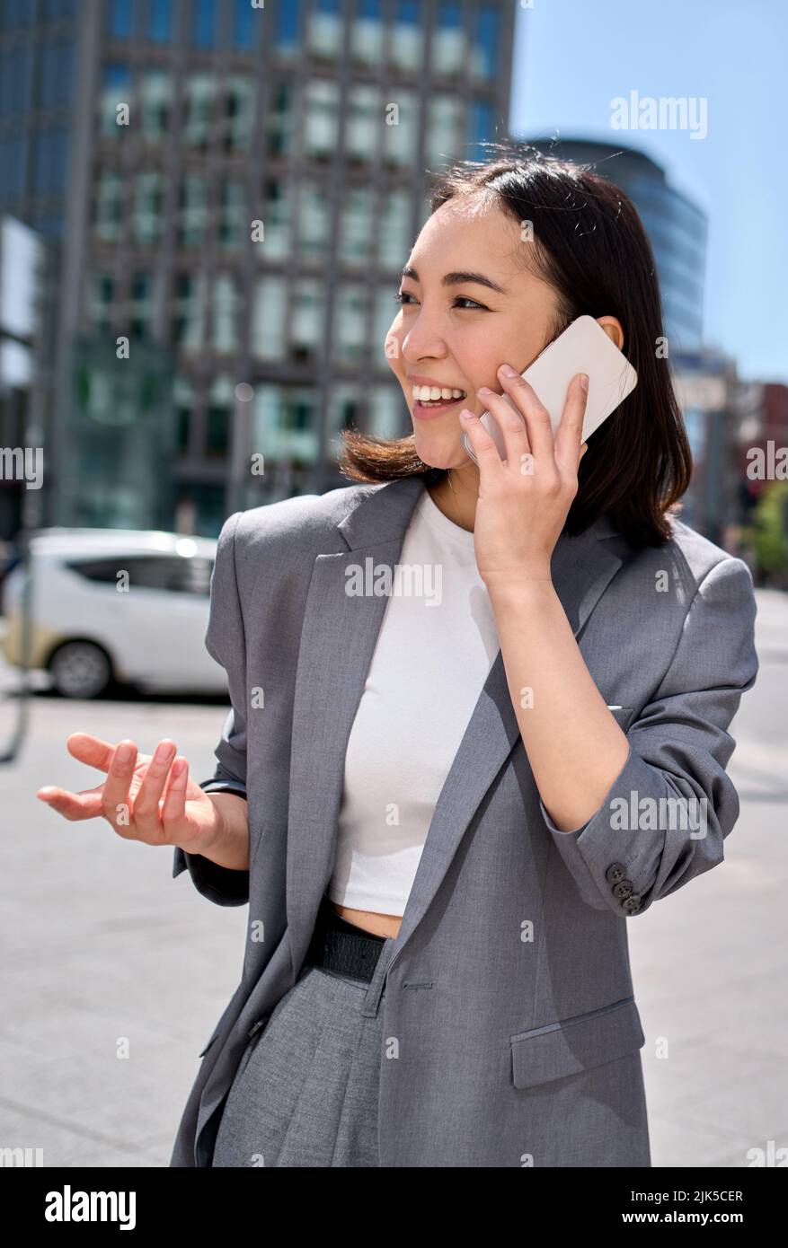 Jeune femme d'affaires asiatique heureuse porte son costume parlant au téléphone dans la rue de la ville. Banque D'Images