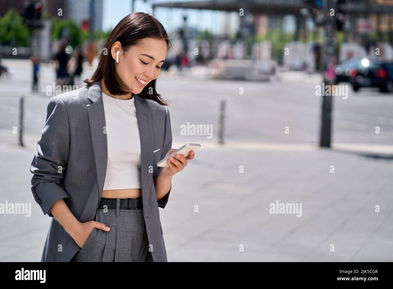 Une jeune femme d'affaires asiatique porte un costume debout dans la rue en utilisant le téléphone. Banque D'Images