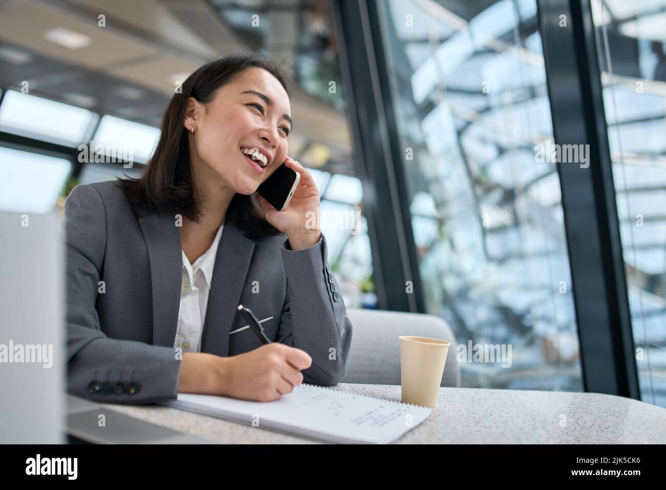 Jeune femme d'affaires chinoise gaie qui parle au téléphone et qui travaille au bureau. Banque D'Images