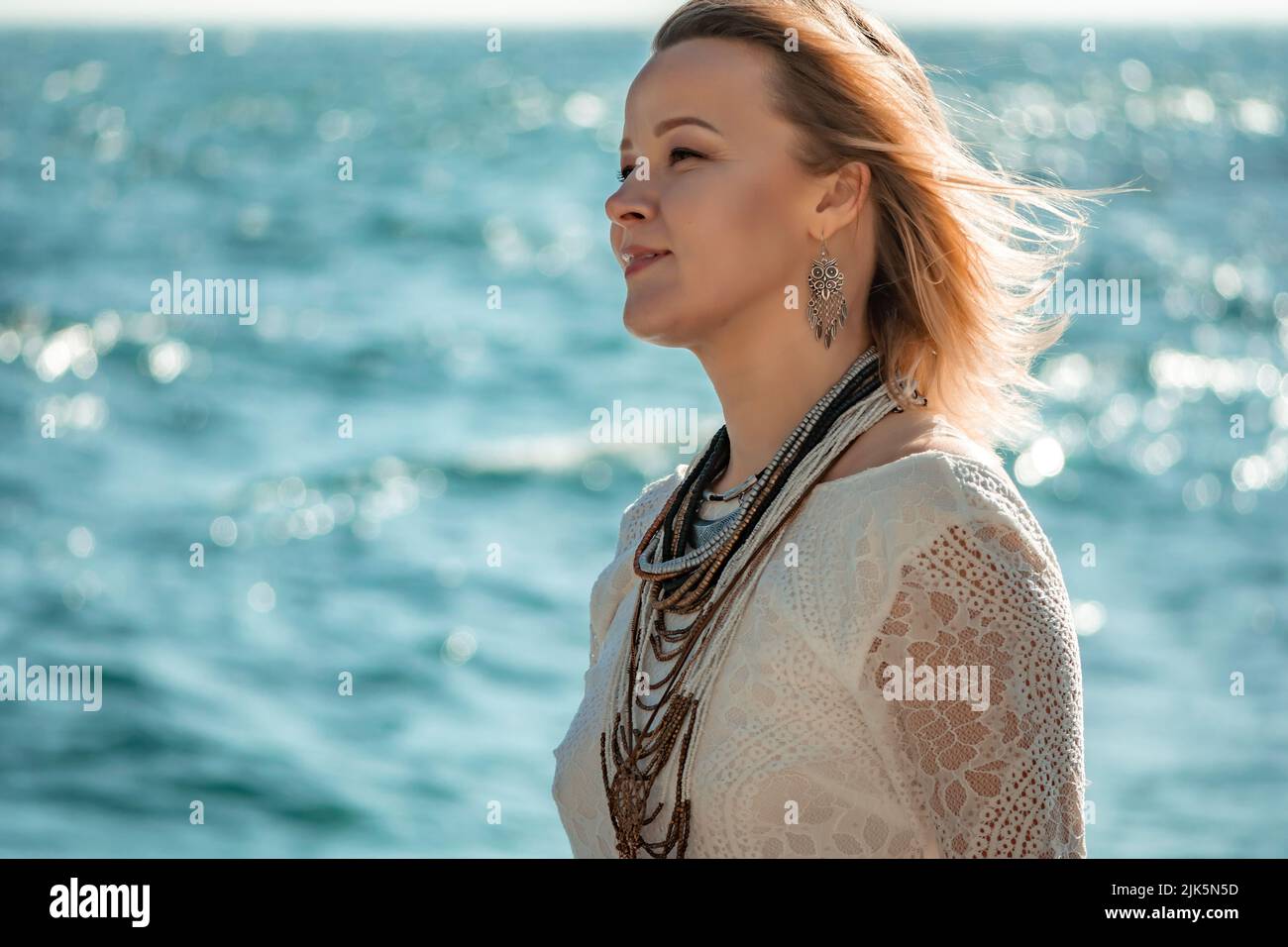 Femme vêtue de bohème sur la plage au coucher du soleil. Style bohémien pour un look tendance sur la station. Femme d'âge moyen bien regardant en robe blanche et style boho Banque D'Images