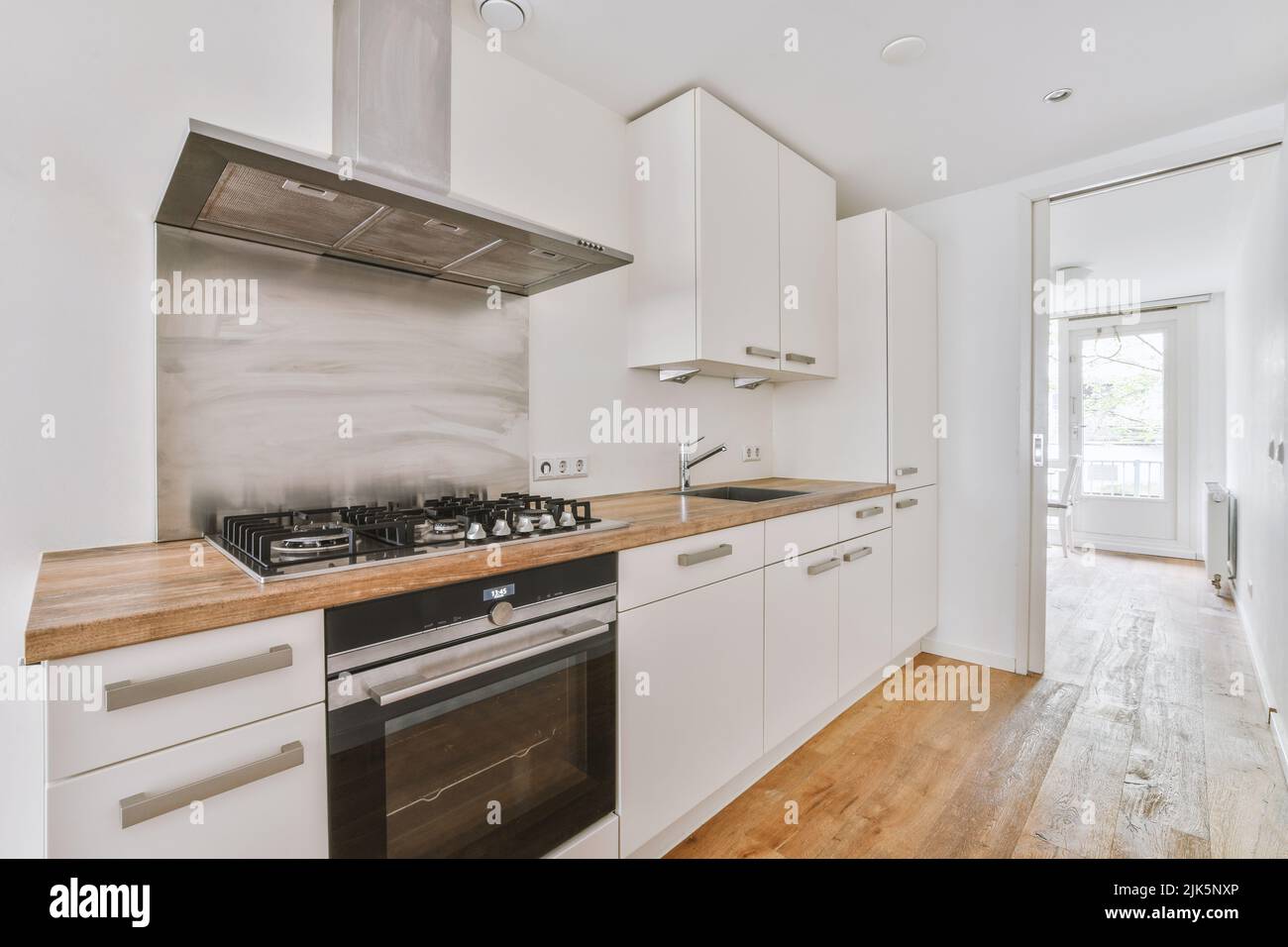 Décoration intérieure contemporaine minimaliste de ce studio lumineux avec table et chaises en bois dans la salle à manger entre la cuisine ouverte et le salon avec murs blancs et parquet Banque D'Images