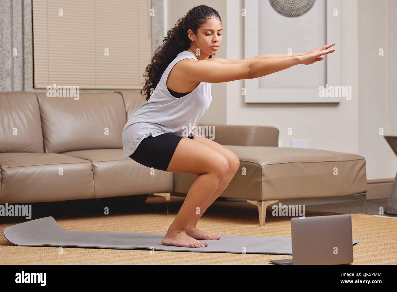 Les cours de fitness en ligne sont les meilleurs. Prise de vue en longueur d'une jeune femme utilisant son ordinateur portable pour suivre un cours de fitness en ligne dans son salon. Banque D'Images