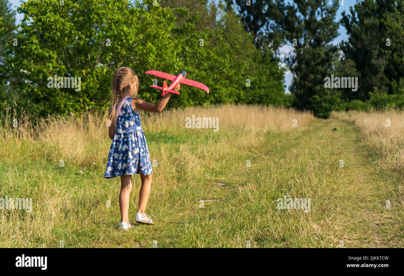 Belle petite fille, courir sur l'herbe et lance un avion de jouet rouge. Un petit enfant s'amuse pendant les vacances d'été. Vacances d'enfance et de voyage Banque D'Images