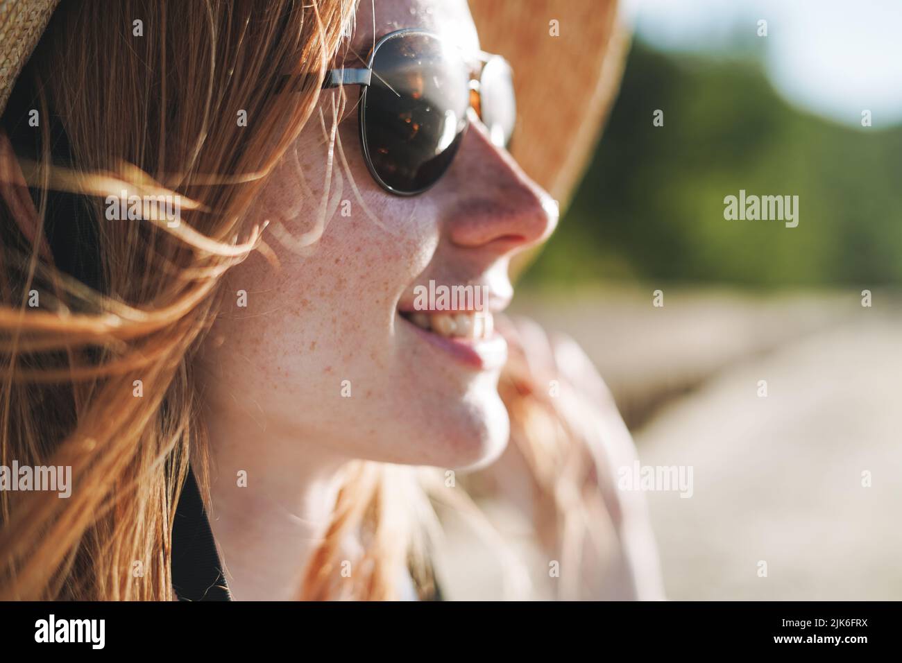 Gros plan de la jeune femme aux cheveux rouges en chapeau de paille et lunettes de soleil sur le paysage du coucher du soleil Banque D'Images