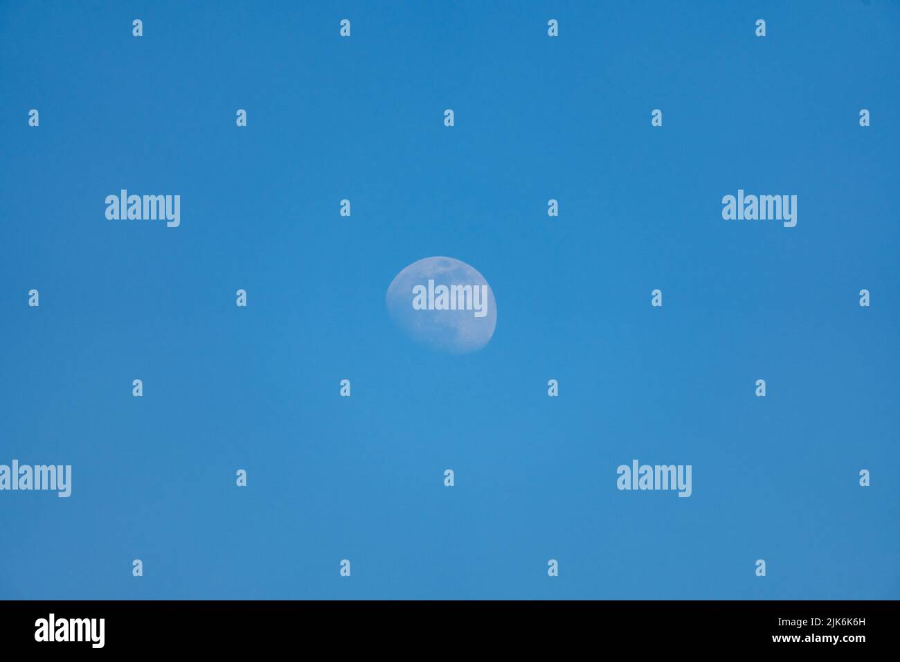 Lune visible le jour avec ciel bleu Banque D'Images