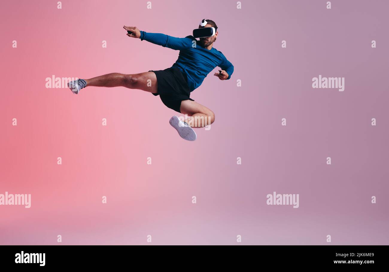 Arts martiaux dans le métaverse. Un jeune sportif qui lance un coup de pied en plein air tout en portant un casque de réalité virtuelle. Jeune homme actif explorant le RE virtuel Banque D'Images