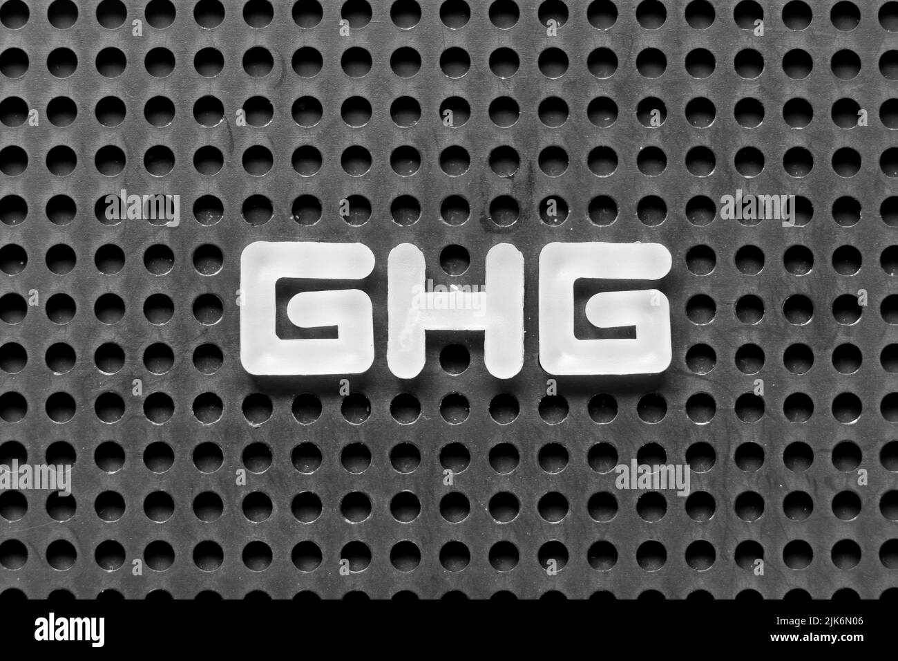 Lettre blanche dans le mot GHG (abréviation de gaz à effet de serre) sur fond perforé noir Banque D'Images
