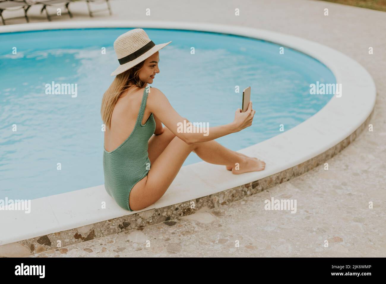 Jolie jeune femme assise près de la piscine et prenant photo selfie avec téléphone mobile dans l'arrière-cour de la maison Banque D'Images