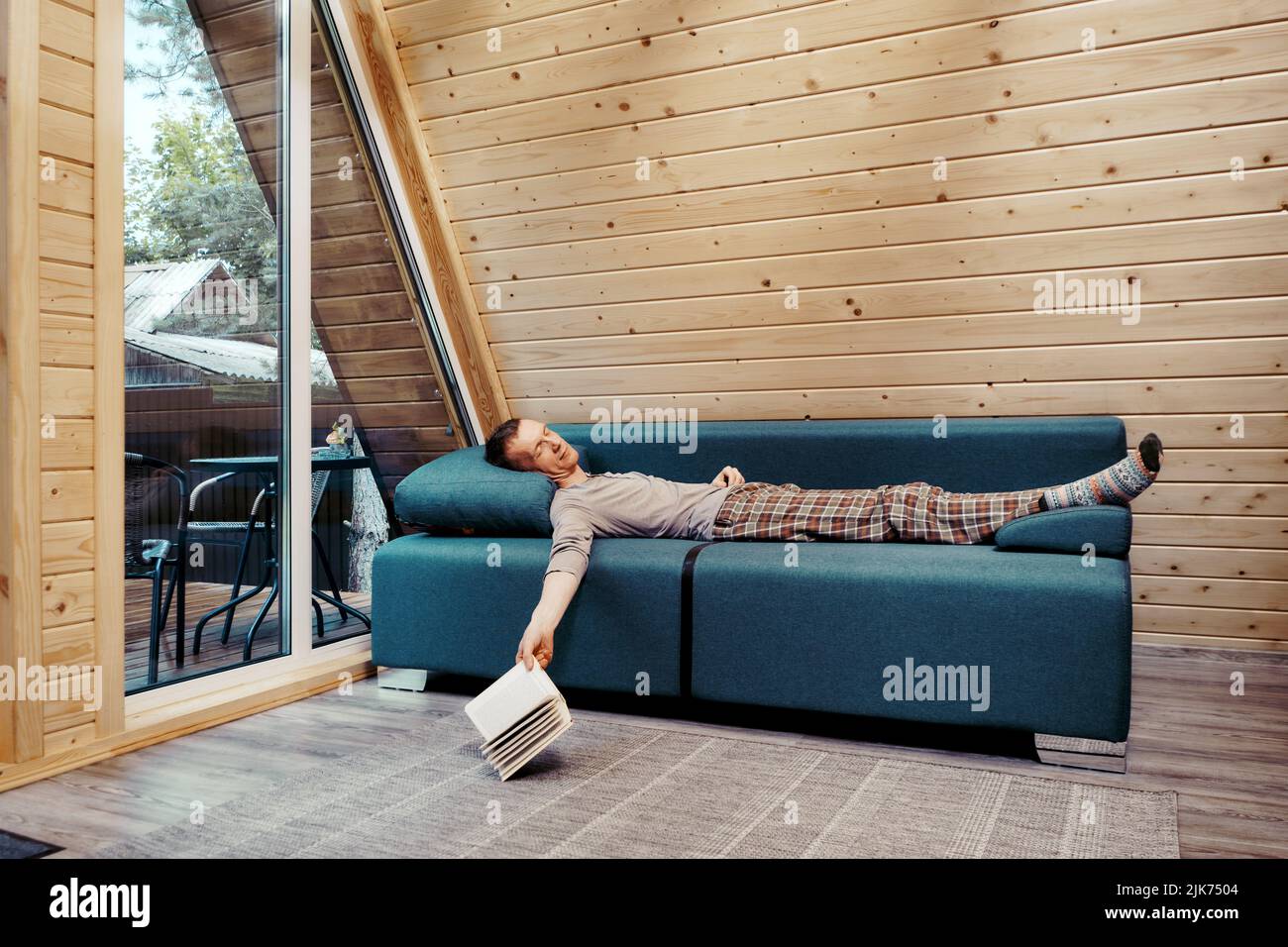 Homme d'âge moyen qui se lit paisiblement sur le canapé de sa maison de campagne. Il a laissé tomber le livre sur le sol. Banque D'Images