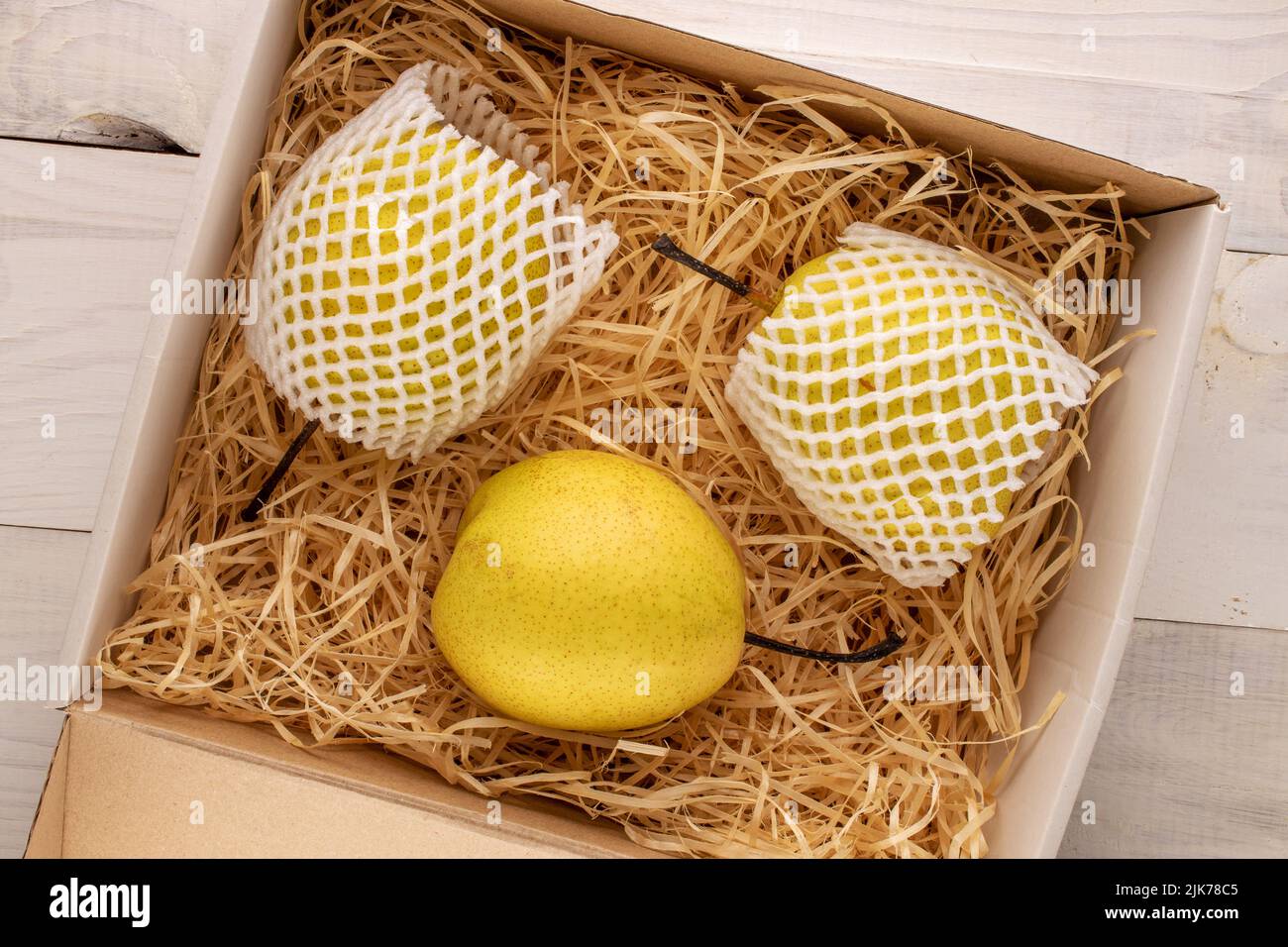 Trois poires jaunes douces dans une boîte avec copeaux de bois sur une table en bois, vue rapprochée du dessus. Banque D'Images
