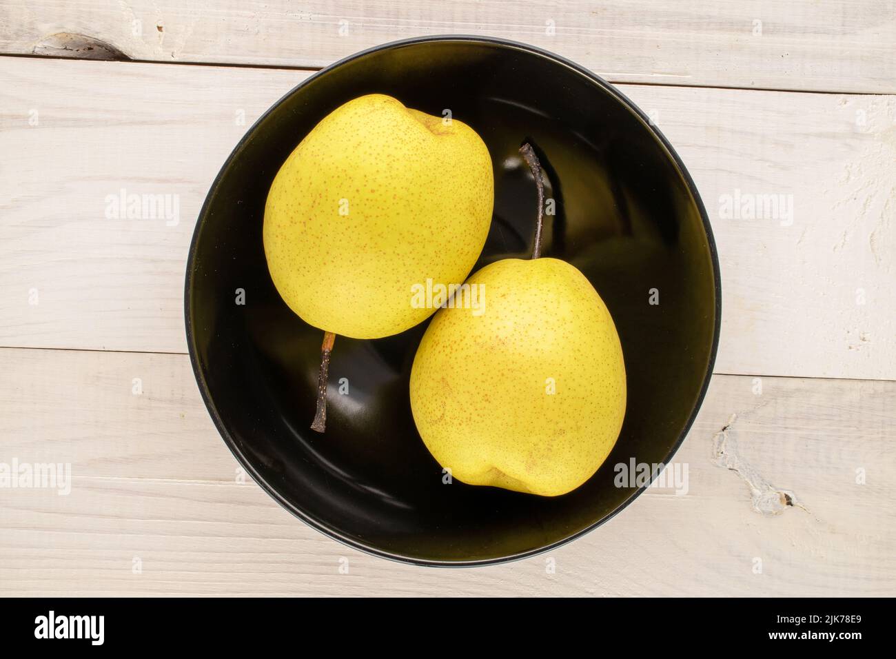 Deux poires jaune vif dans une assiette en céramique noire sur une table en bois, vue rapprochée du dessus. Banque D'Images