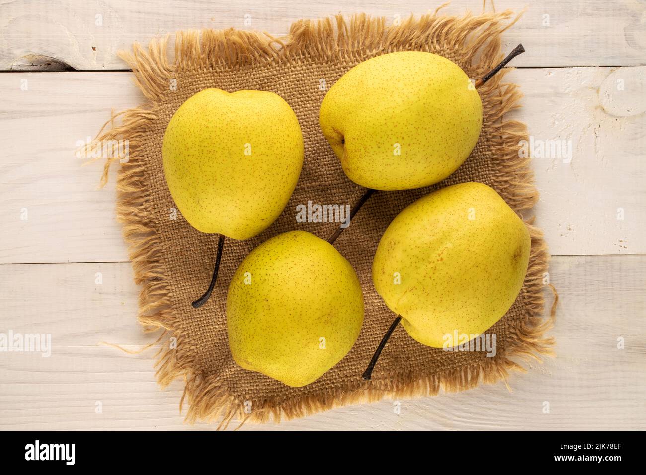 Quatre poires jaunes douces avec une serviette en jute sur une table en bois, vue rapprochée du dessus. Banque D'Images