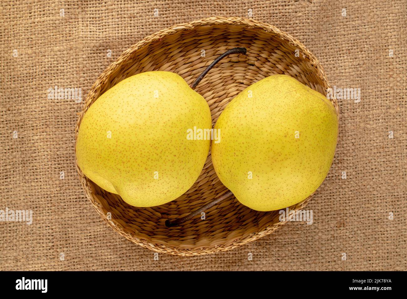 Deux poires jaunes douces et lumineuses avec une assiette de paille en toile de jute, vue rapprochée, vue de dessus. Banque D'Images