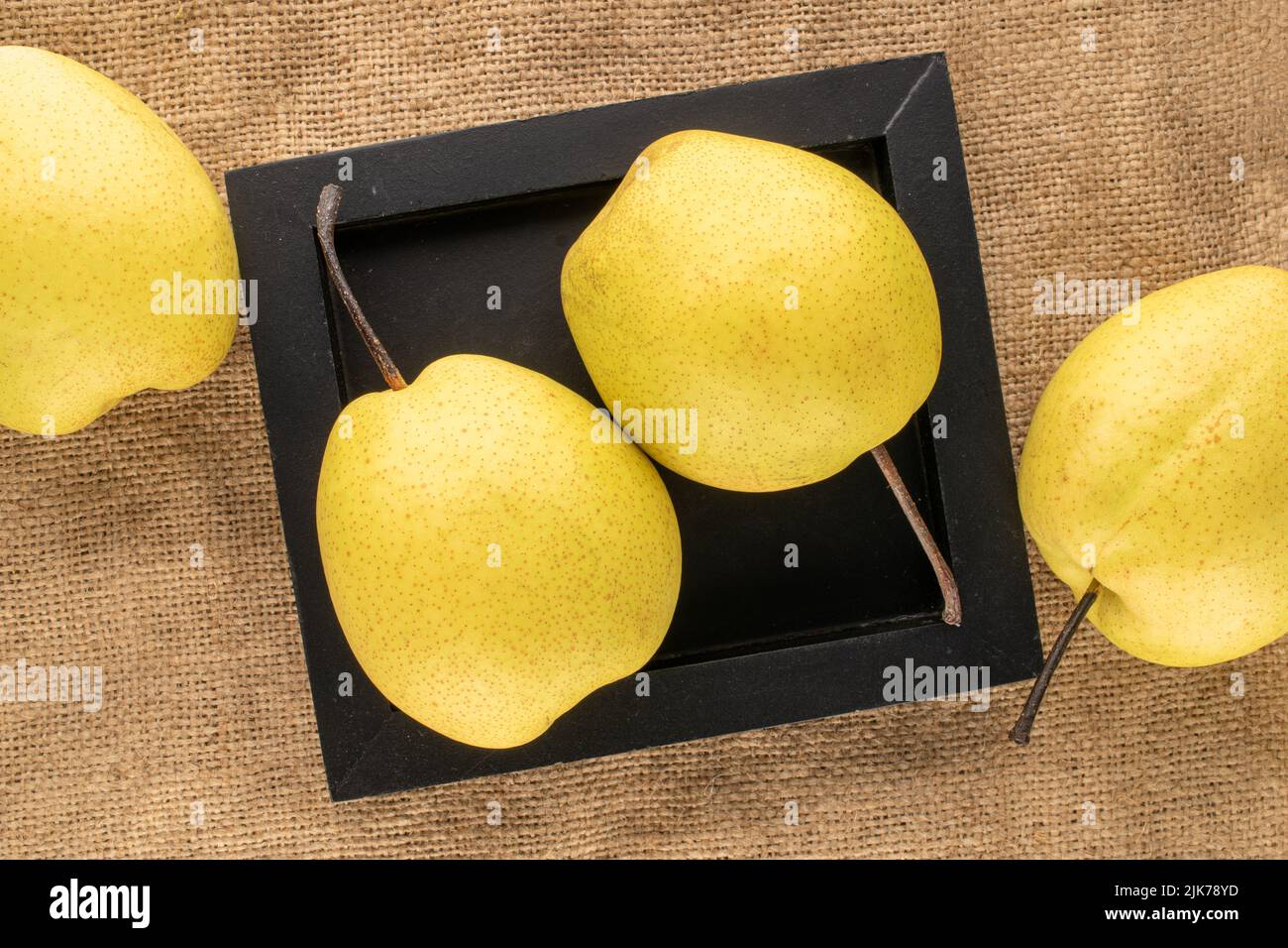 Quatre poires jaune vif avec plateau en bois noir sur toile de jute, vue rapprochée du dessus. Banque D'Images