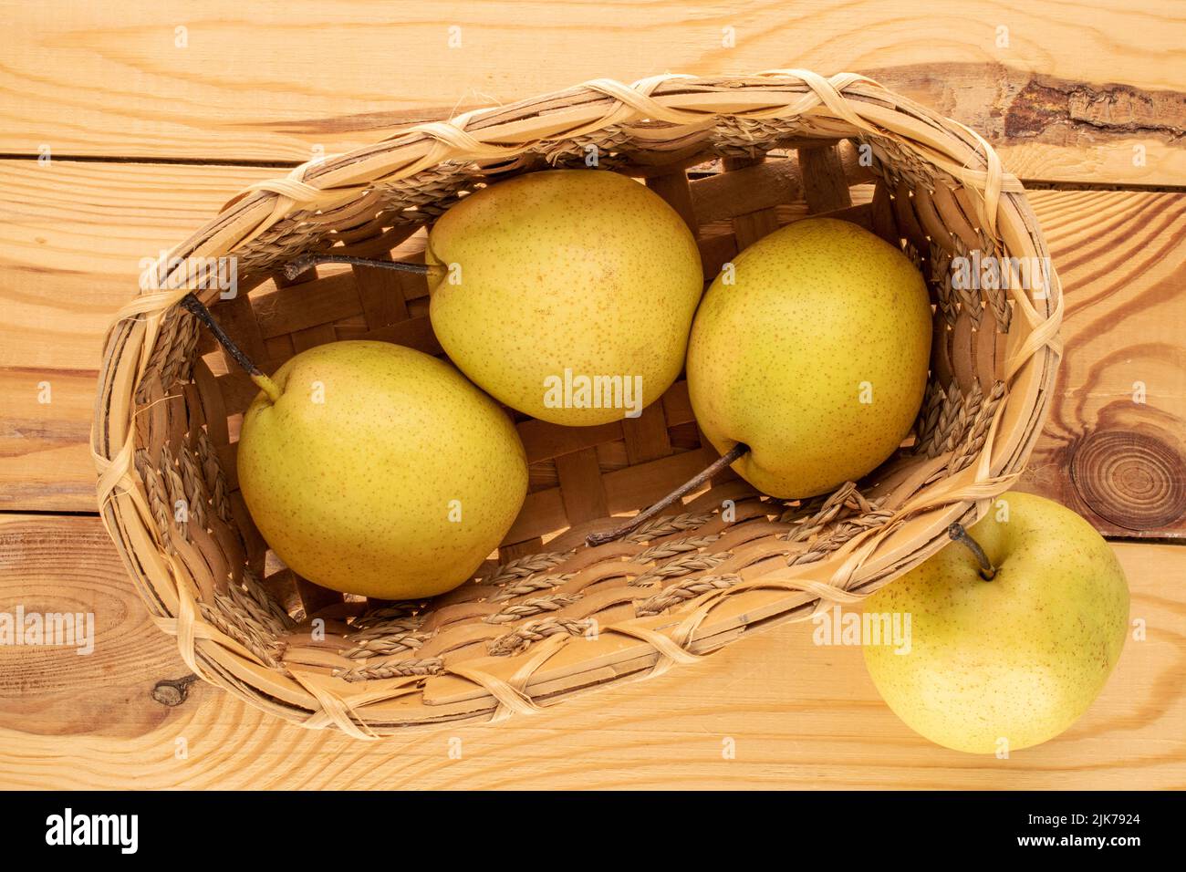 Quatre poires jaune vif dans un panier sur une table en bois, vue rapprochée, vue de dessus. Banque D'Images