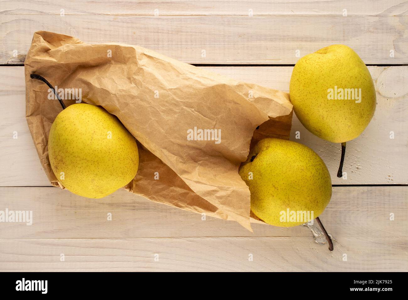 Trois poires jaunes douces avec un sac en papier sur une table en bois, vue rapprochée du dessus. Banque D'Images