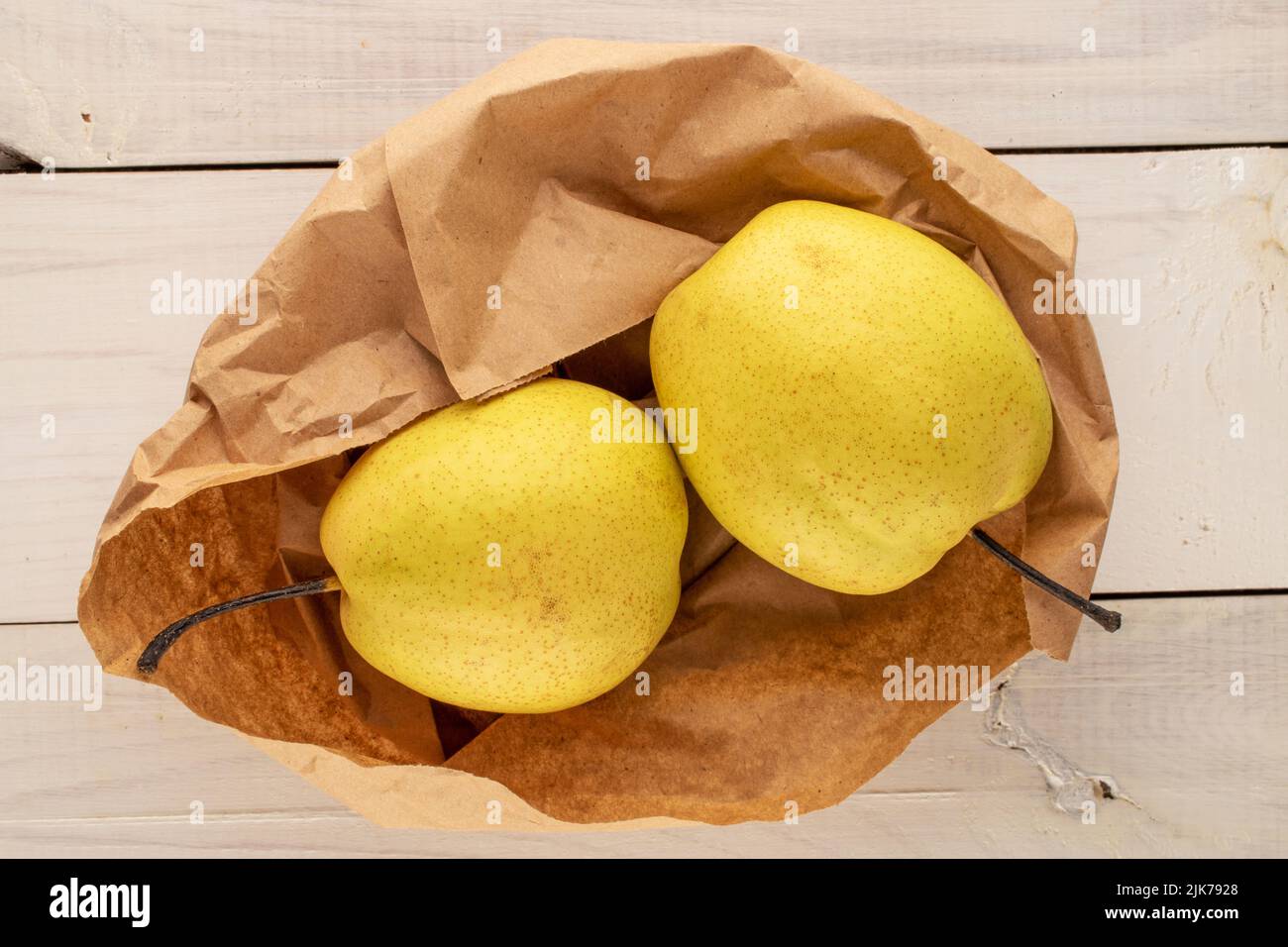 Deux poires jaune vif avec un sac en papier sur une table en bois, vue rapprochée du dessus. Banque D'Images