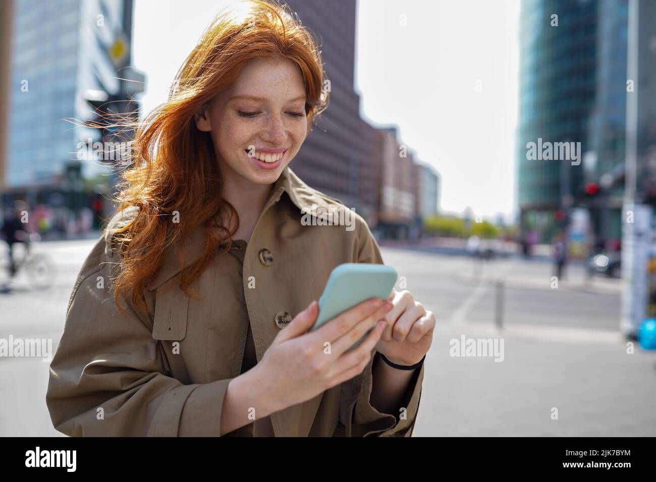 Bonne adolescente redhead debout sur la grande ville urbaine rue en utilisant le smartphone. Banque D'Images
