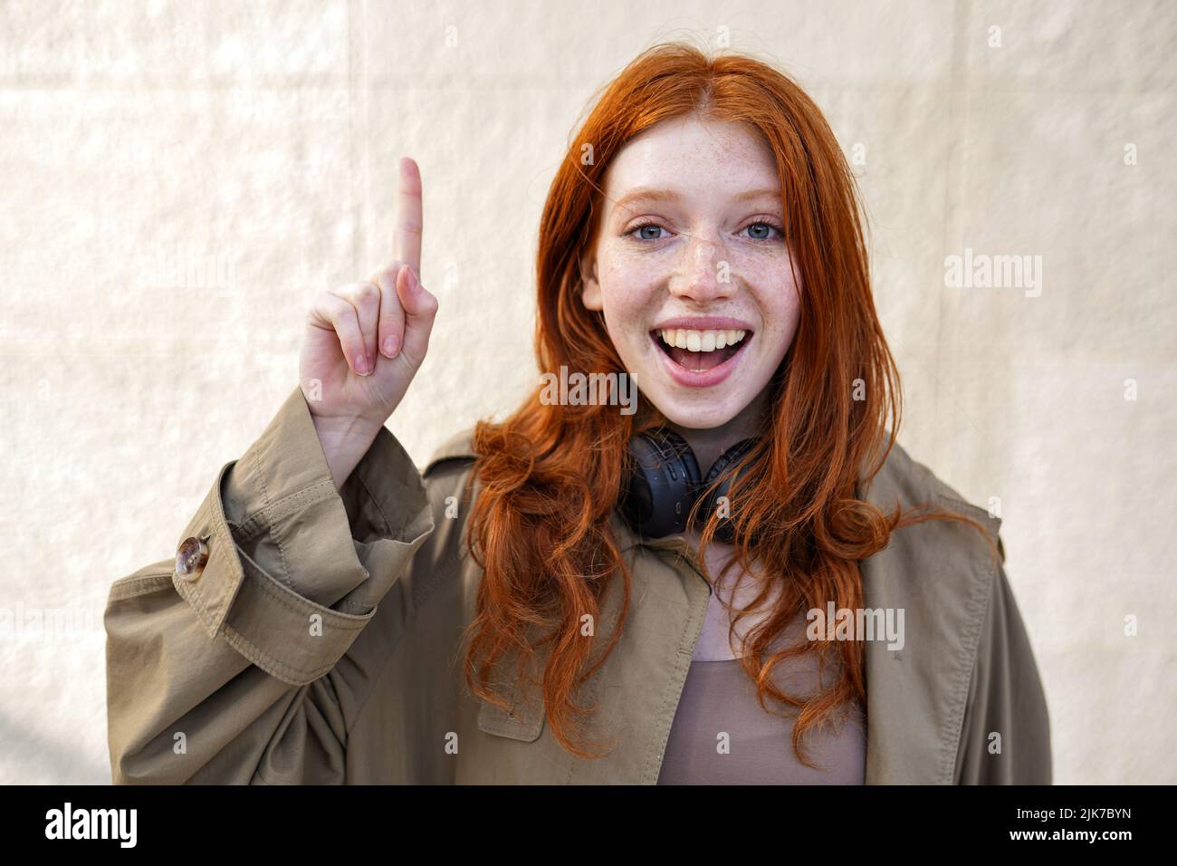 Bonne adolescente redhead debout sur fond de mur urbain pointant vers le haut. Banque D'Images