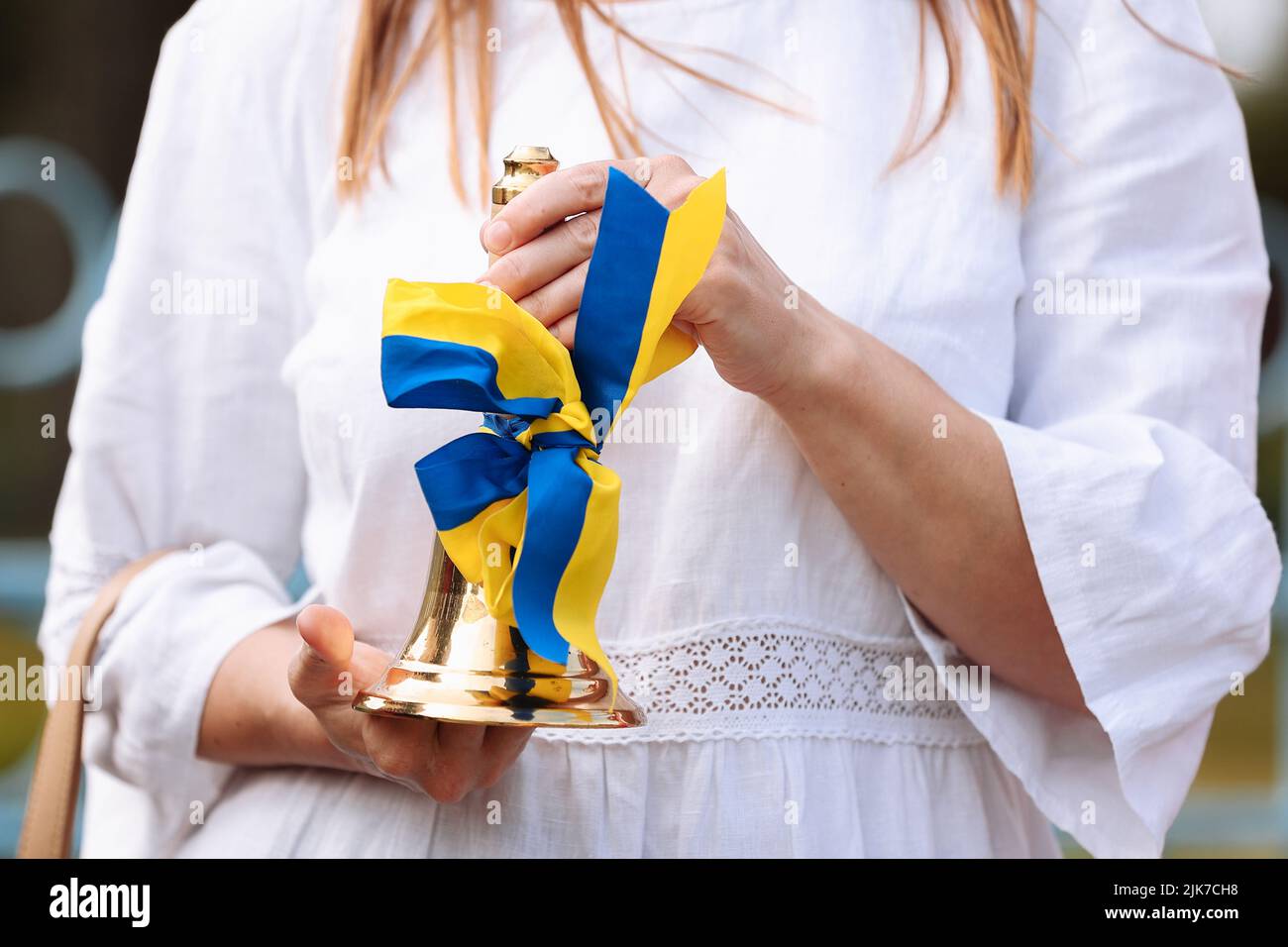 Photo rognée des mains des femmes tenant la cloche de l'école avec un arc jaune bleu - un symbole du début de l'année scolaire ou de la remise des diplômes en Ukraine. Conc Banque D'Images