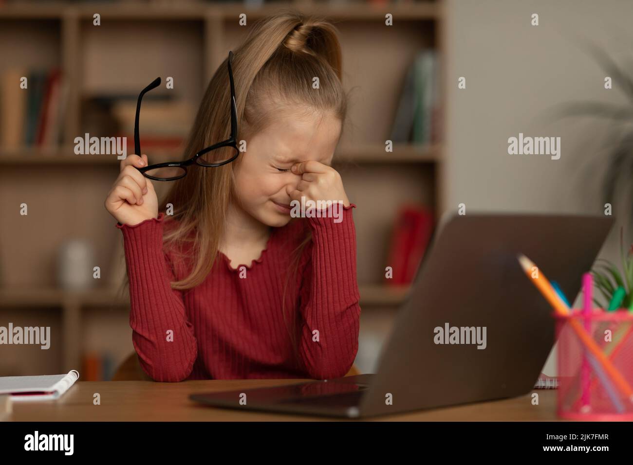 Fille qui prend des lunettes ayant une mauvaise vue près d'un ordinateur portable intérieur Banque D'Images