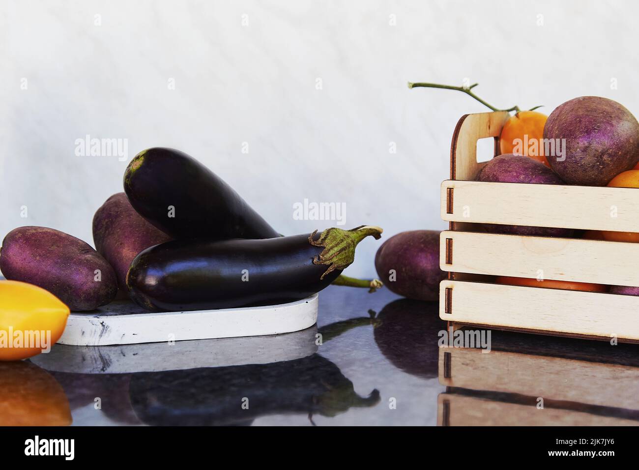 Légumes de saison dans une boîte en bois et sur des podiums - tomates fraîches, pommes de terre pourpres, aubergines. Préoccupations écologiques, achats écologiques. Marché alimentaire équitable Banque D'Images