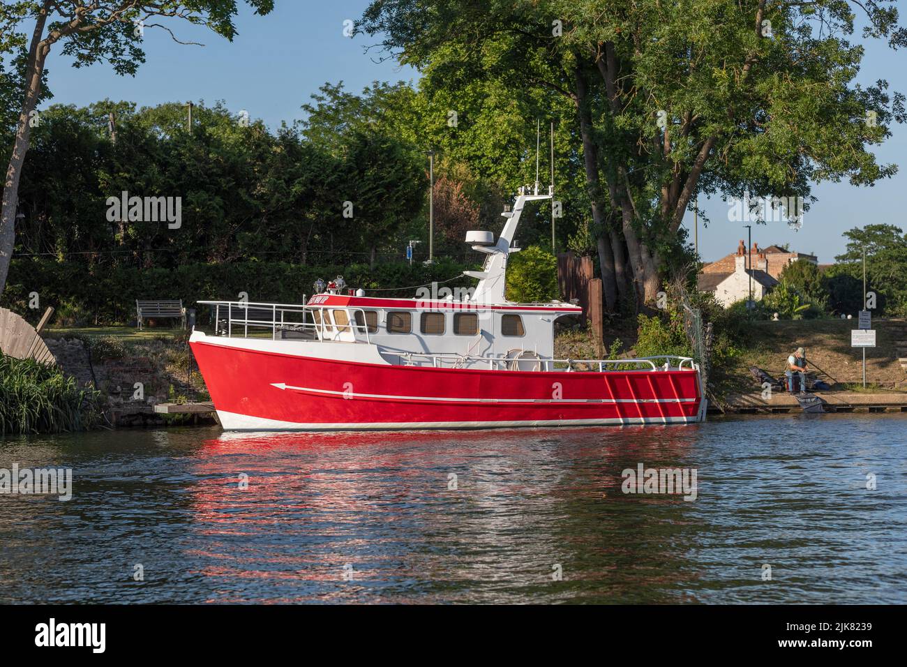 Un bateau à coque d'acier peint en rouge et blanc, amarré sur la rive de la Tamise en plein soleil en été à Surrey, en Angleterre Banque D'Images