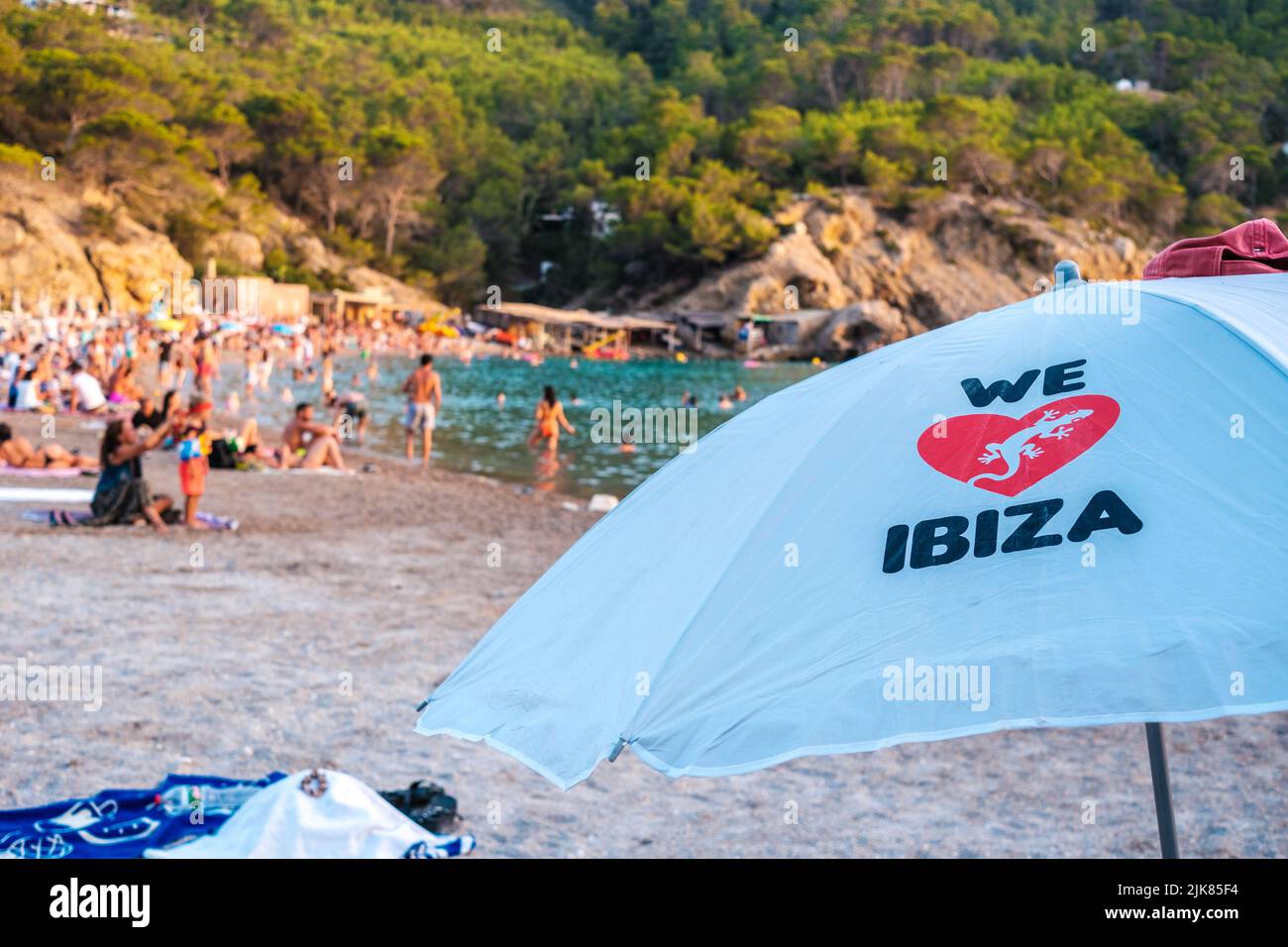 Ibiza, espagne - 25 juillet 2022: Parapluie de plage avec nous aimons texte Ibiza sur une plage avec des vacanciers défocused en arrière-plan. Banque D'Images