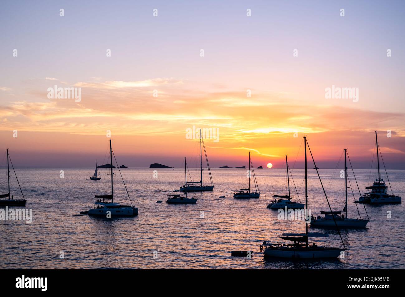 Plusieurs yachts et bateaux ancrés près de la côte se détendent en regardant le coucher du soleil à l'horizon des îles méditerranéennes. Banque D'Images